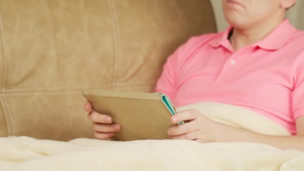 Jeune homme avec tablette assis sous les couvertures sur le canapé — Video