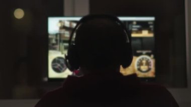 Kafasında kulaklık olan genç bir adamın silueti, monitörün arka planı, karanlık bir gece çalıyor.