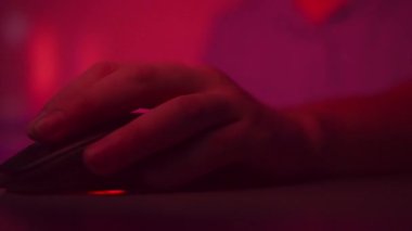 Close up man hand holds a computer mouse, clicks on buttons, multicolored lighting