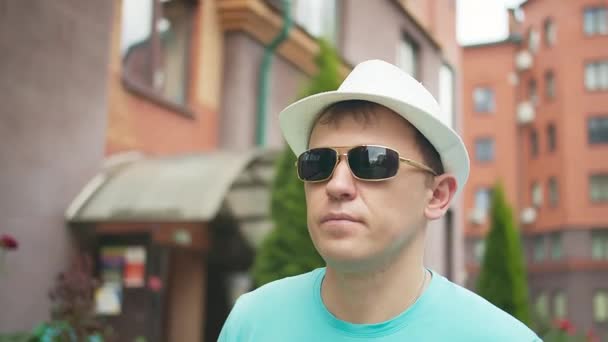 Retrato de un hombre con sombrero y gafas de sol pasea por la calle de la ciudad, rastreando cámaras — Vídeos de Stock