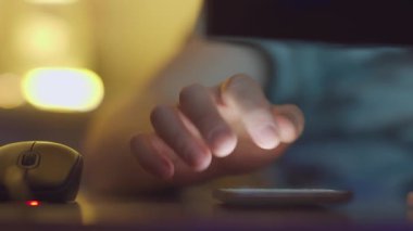 Bir adam evde bilgisayarla çalışıyor ve cep telefonundaki mesajlara cevap veriyor.