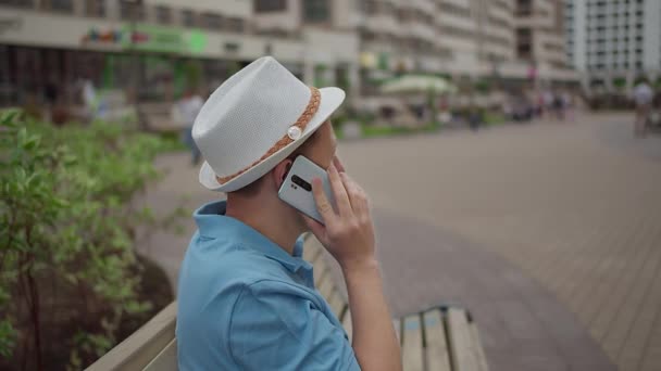En man sitter på en bänk och pratar på en mobiltelefon — Stockvideo