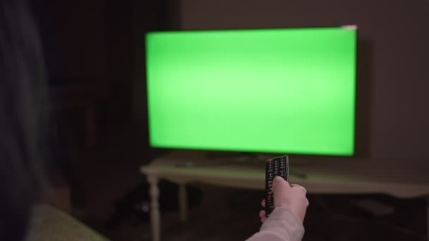 The girl is sitting in front of the TV in the evening with a remote control in her hand, chroma key — Stock Video