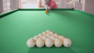 Adam bilardo oynuyor, top piramidini kırıyor, odaklanıyor.