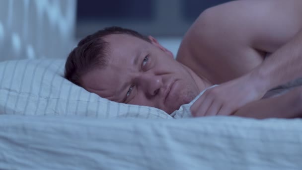 Lying in bed at night, a man cannot sleep, covers his head with a pillow — Stock Video