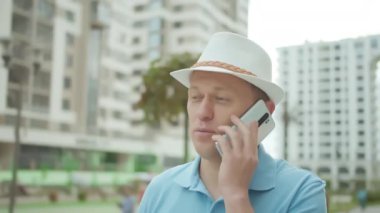 Bir adam şehir caddesinde dururken cep telefonuyla konuşuyor.