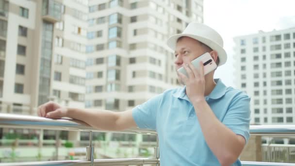 Молодой человек разговаривает по мобильному телефону на фоне небоскребов — стоковое видео