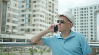 Şapkalı kendine güvenen bir adam cep telefonuyla konuşuyor çitlerin yanında duruyor, kamera hareketi