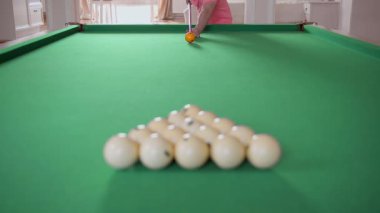 Bir adam bilardo oynuyor, ıstakayla topa vuruyor, üçgen şeklinde top kırıyor.