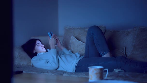 Fille nuit adolescente se trouve sur le canapé avec un téléphone portable dans ses mains, ne peut pas dormir — Video