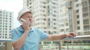 Şapkalı bir adam cep telefonuyla konuşuyor, gökdelenlerin arka planında, kamera takibi...