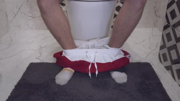 Egy zoknis fiatalember lábai, aki kijött a WC-re és leült a WC-re. — Stock videók