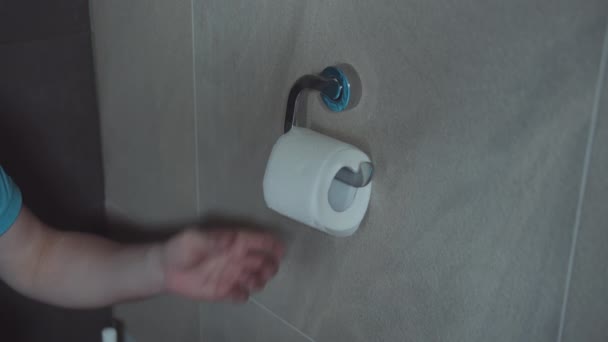 Man sitting in the toilet tears off toilet paper from a roll — Stock Video