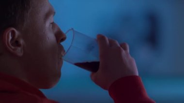 Geceleri adam TV 'de oturur, gazoz içer ve film izler, renkli yansımalar, yakın çekim.