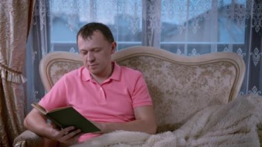 Akşamları kanepede otururken kitap okuyan çekici bir adam.