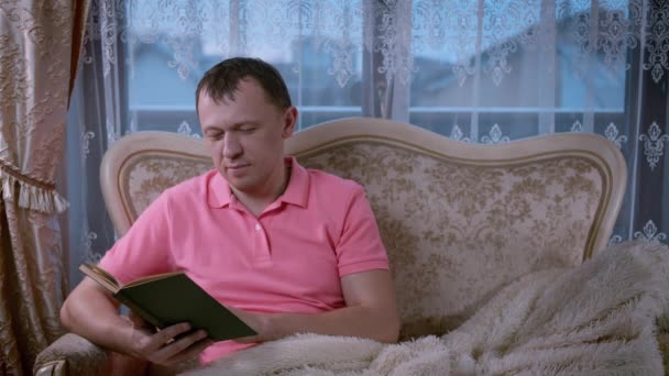 Привабливий чоловік читає книгу, сидячи ввечері на дивані — стокове відео