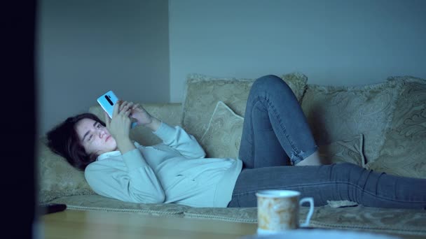 Adolescente se couche sur le canapé la nuit avec un téléphone dans ses mains — Video