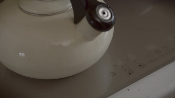 Silbando hervidor de agua se coloca en una cocina de inducción, un hombre se enciende con el dedo, cocinar — Vídeo de stock