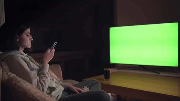 Chica morena sentada en el sofá, viendo la televisión y jugando juegos móviles, croma key — Vídeos de Stock