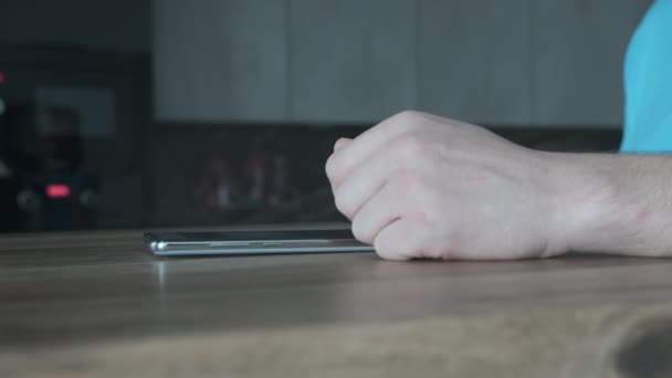 Il telefono si trova su un tavolo di legno, un uomo muove il dito attraverso lo schermo — Video Stock