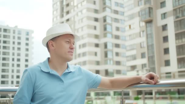 Un turista en un sombrero se para en una valla de metal, pone su mano sobre la barandilla, mira a su alrededor — Vídeos de Stock