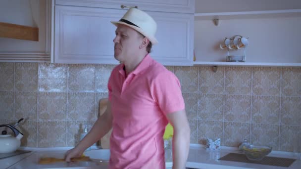 El hombre se divierte en el fondo de la cocina, toma una espátula de madera, canta una canción y baila — Vídeo de stock