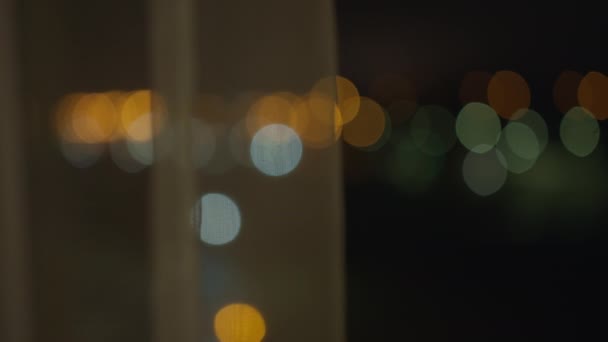 Luci sfocate della città di notte da una finestra aperta, dietro le tende — Video Stock