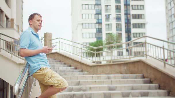 Muž stojí na schodech v očekávání setkání, v rukou mobilního telefonu, kopírovat prostor — Stock video