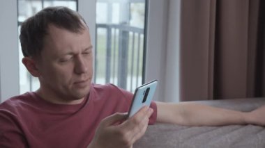 Adam mesajları okuyor, internette akıllı telefondan geziniyor, kanepede oturuyor.