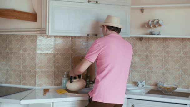 Man heeft plezier op de achtergrond van de keuken, zingt een lied giet water in een waterkoker — Stockvideo