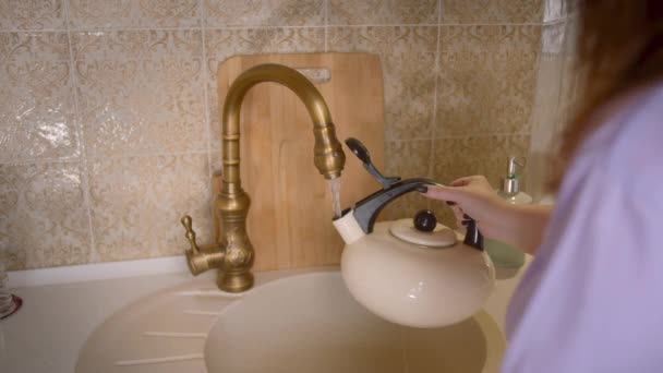 가정 옷을 입고 있는 여자 가수 도 꼭지에서 물을 빨아들여 주전자에 담는다 — 비디오