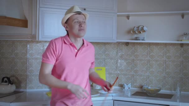 Un homme s'amuse sur le fond de la cuisine, prend une spatule, chante une chanson et danse — Video