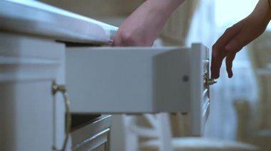 Bir kadının eli çekmeceyi çatalla açar ve yemek için masaya gider.