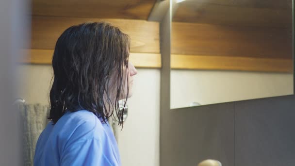 Girl stands in front of the bathroom mirror, dries her hair with a hairdryer, camera tracking — Stock Video