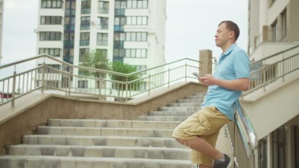 Mann steht auf der Treppe in Erwartung eines Treffens, in den Händen eines Mobiltelefons, Kamerabewegung — Stockvideo