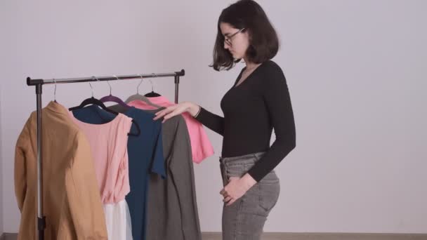 Una adolescente elige la ropa del estante, elige un vestido rosa, se prueba a sí misma — Vídeos de Stock