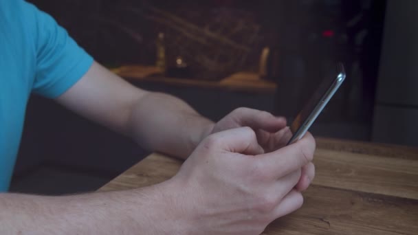 A man with a mobile phone in his hands, sits at a wooden table, uses an application — Stock Video