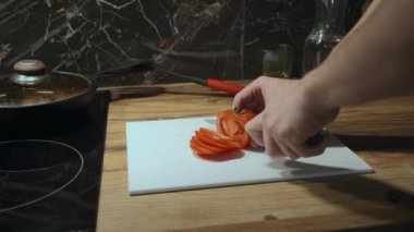 Adam akşamları mutfakta yemek hazırlıyor, domatesi dilimliyor.