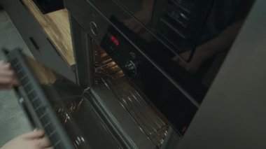 Bir adam fırının kapısını açar ve tepsiye büyük bir pizza koyar. Yemek pişirmek, yemek pişirmek, odaklanmak, üst manzara için.