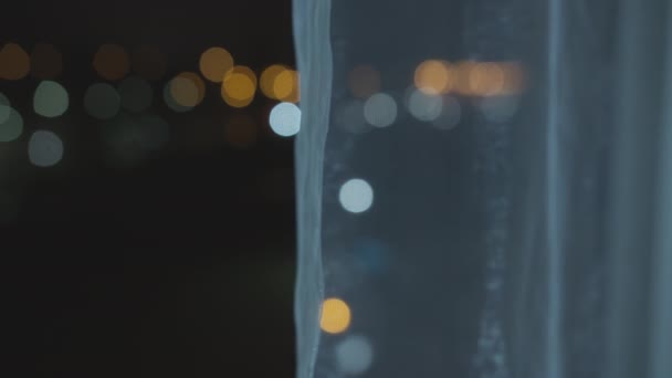 Luces borrosas de la ciudad nocturna desde una ventana abierta, desde detrás de las cortinas — Vídeo de stock