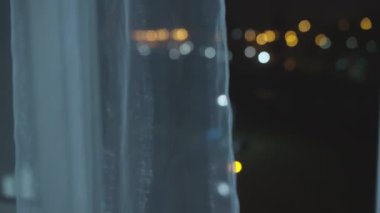 Gece şehrinin çok renkli ışıkları açık bir pencereden, perdelerin arkasından, bulanık