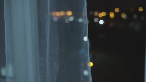 Bunte Lichter der nächtlichen Stadt aus einem offenen Fenster, hinter Vorhängen, verschwommen — Stockvideo