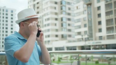 Beyaz şapkalı bir adamın portresi telefonda konuşuyor, güneş gözlüğünü çıkarıyor.