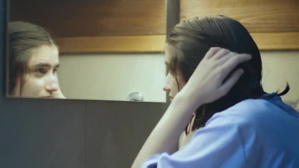 Chica con el pelo mojado se para delante del espejo en el baño, mira a su reflejo — Vídeos de Stock