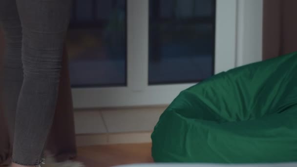 Girl teenager in the evening in her room sits down to rest on a beanbag, camera tracking — Stock Video