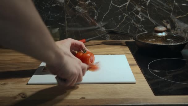 Um homem prepara o jantar na cozinha à noite, corta um tomate em fatias. — Vídeo de Stock