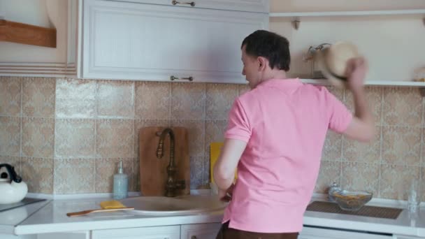 Ένας άντρας με ροζ μπλουζάκι και φοράει καπέλο χορεύει και τραγουδάει στην κουζίνα. — Αρχείο Βίντεο