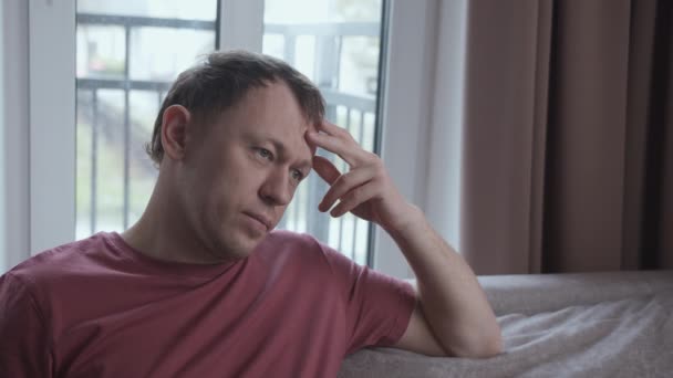 Portrait of serious man on sofa, negative emotions, window background — 图库视频影像