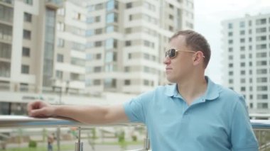 Güneş gözlüklü adam metal parmaklıkların yanında duruyor.