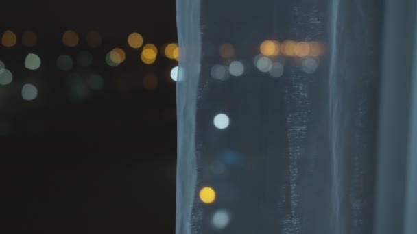 Lichter der nächtlichen Stadt aus einem offenen Fenster, hinter Vorhängen, verschwommener Hintergrund — Stockvideo